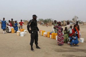 A Cameroonian police officer stands next to people waiting to fill jerrycans with water at the Minawao refugee camp for Nigerians who have fled Boko Haram attacks in Minawao, Cameroon, March 15, 2016. REUTERS/Joe Penney