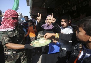 A masked Palestinian distributes sweets as he celebrates with others an attack on a Jerusalem synagogue, in Rafah in the southern Gaza Strip November 18, 2014.  Two Palestinians armed with a meat cleaver and a gun killed four people in a Jerusalem synagogue on Tuesday before being shot dead by police, the deadliest such incident in six years in the holy city amid a surge in religious conflict. REUTERS/Ibraheem Abu Mustafa (GAZA - Tags: POLITICS CIVIL UNREST)